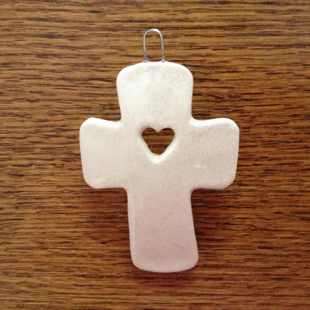 A cross with a heart on it is hanging from the side of a wooden table.