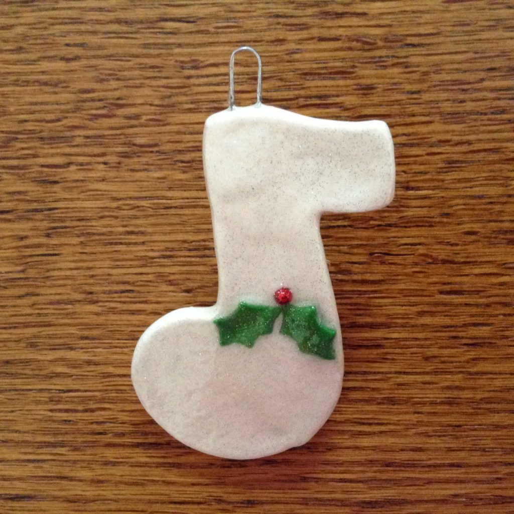 A white christmas stocking ornament with holly on it.