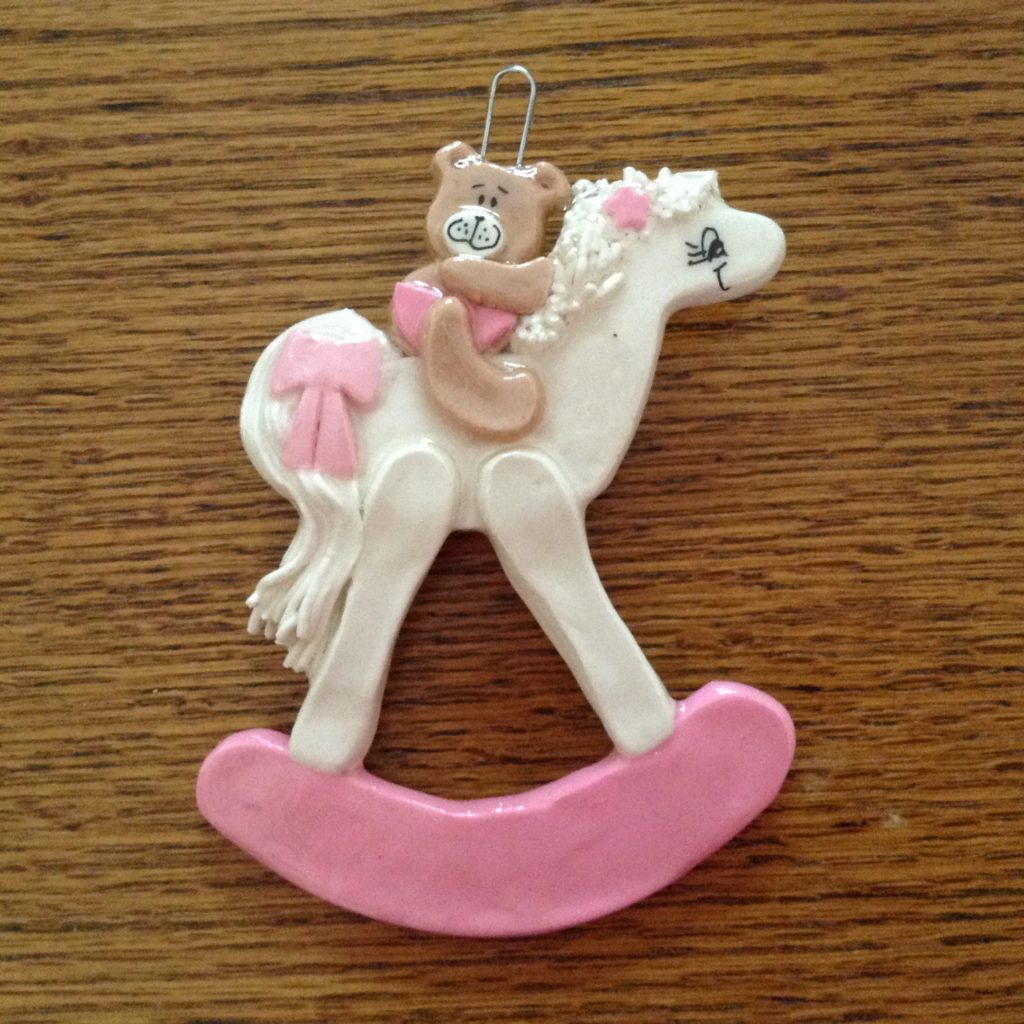 A white and pink rocking horse ornament with a girl on it.
