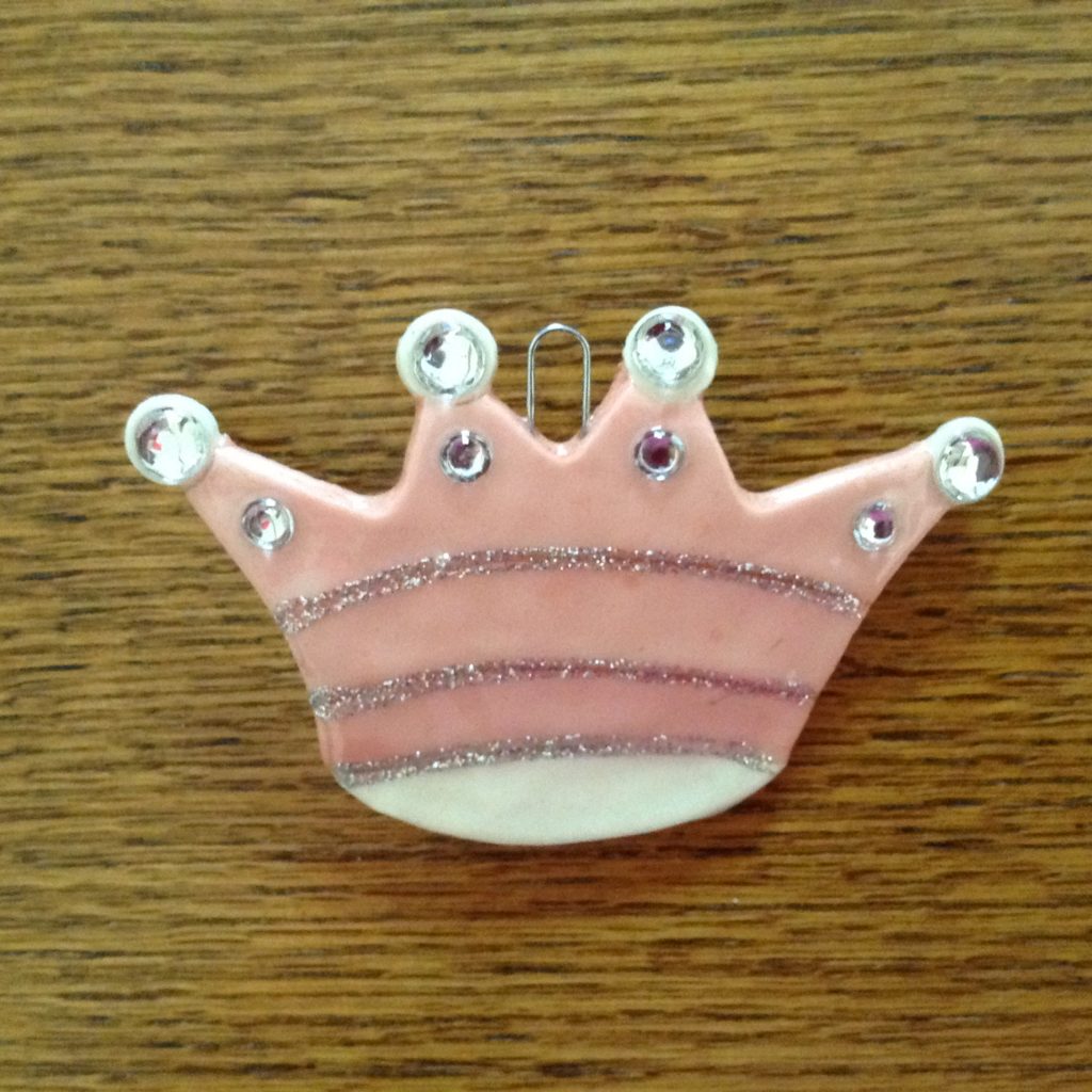 A pink crown with white stripes and silver rhinestones.