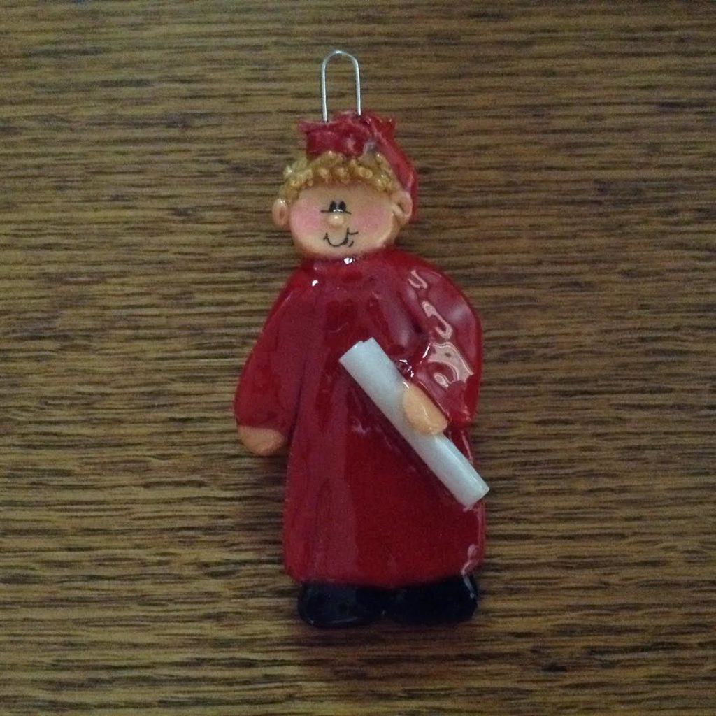 A red ornament with a girl in a robe holding a white stick.