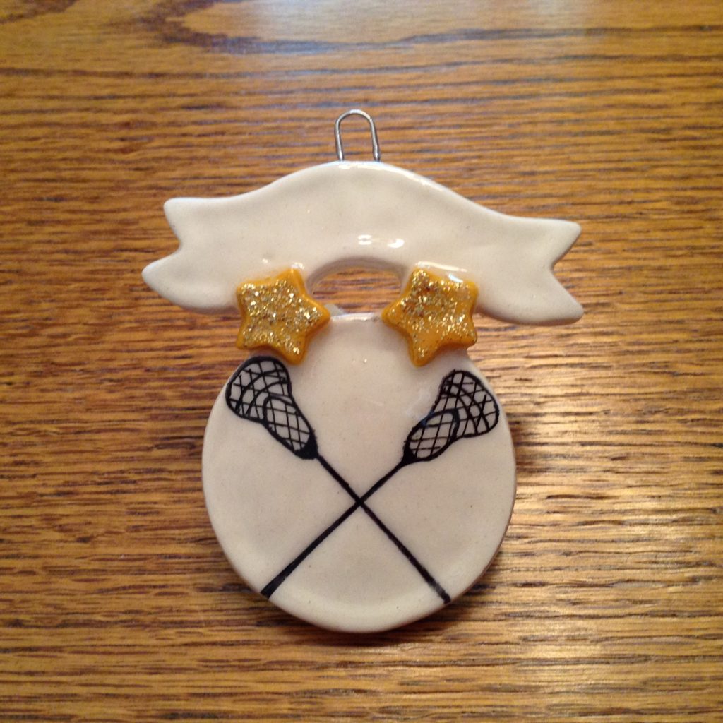 A white ornament with two lacrosse sticks and gold stars.