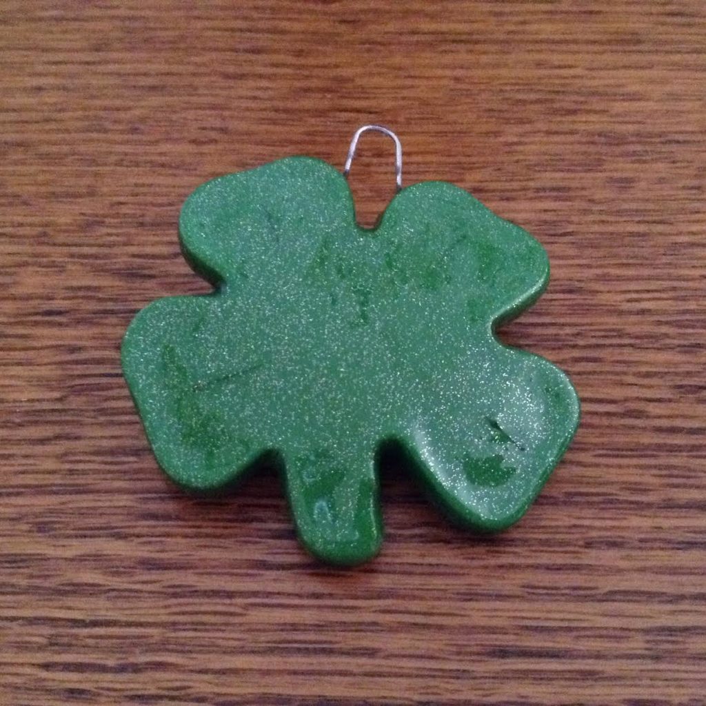 A green shamrock shaped clay ornament on top of a wooden table.