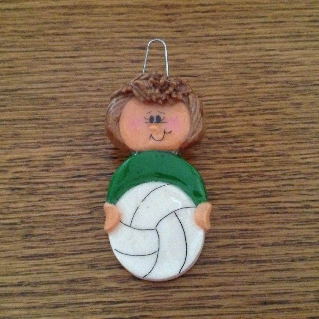 A small clay figure of a boy holding a volleyball.