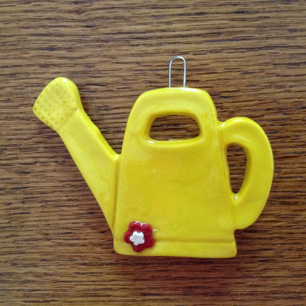 A yellow watering can ornament on a wooden surface.