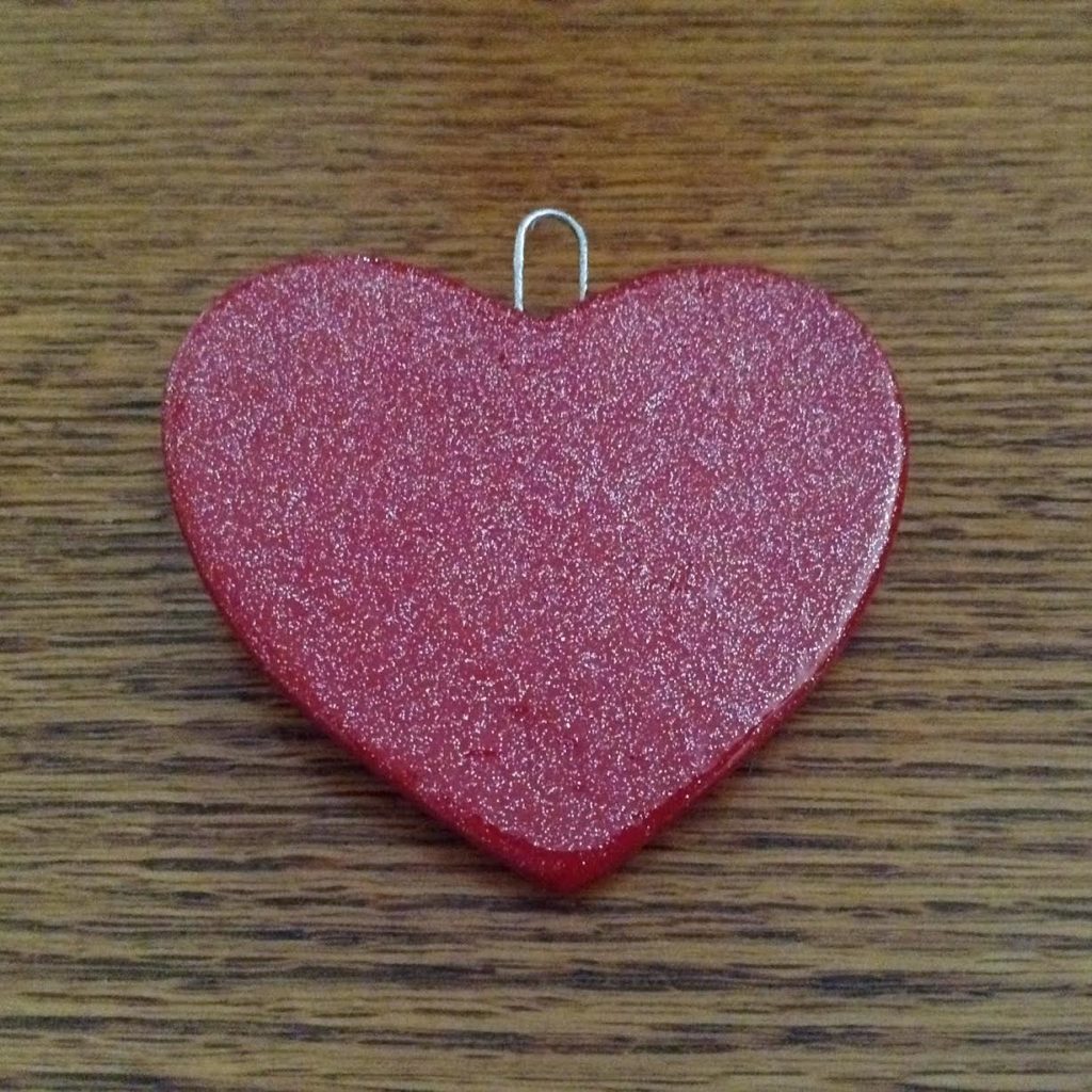 A red heart shaped pendant on top of a wooden table.