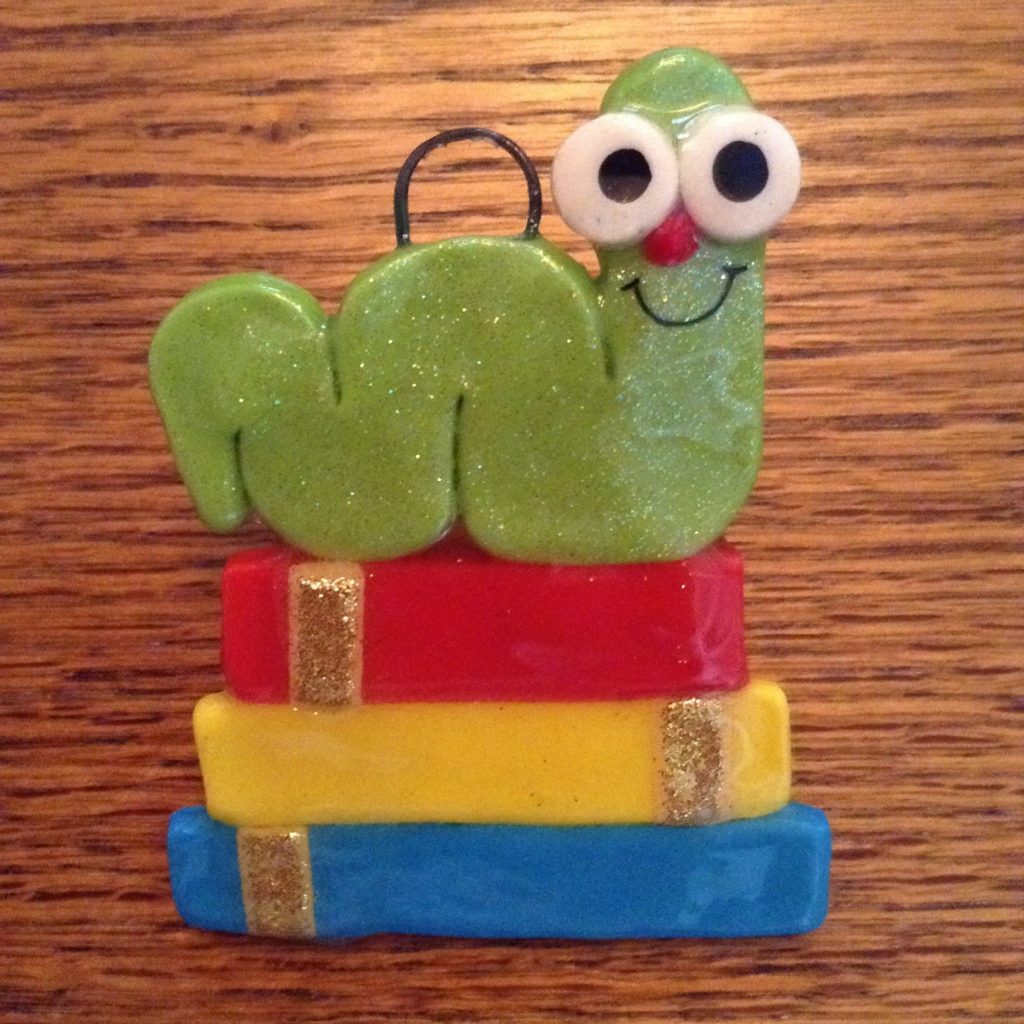 A wooden table with a green caterpillar on top of books.