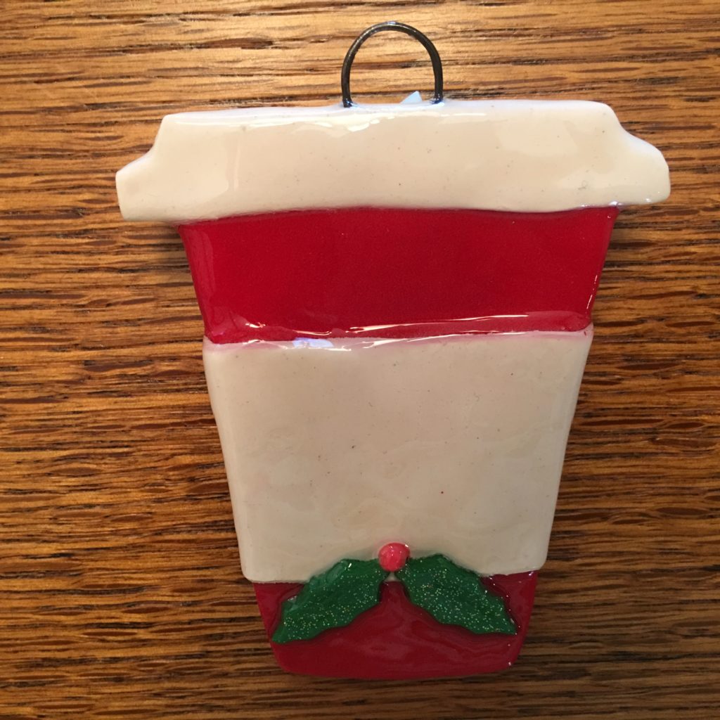 A red and white cup ornament with holly leaves.