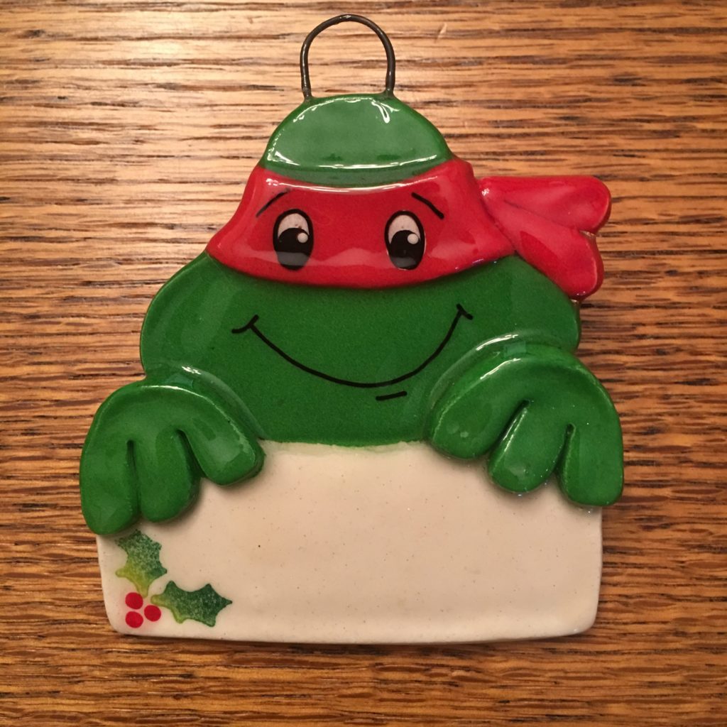 A green frog with a red hat and holding a sign.