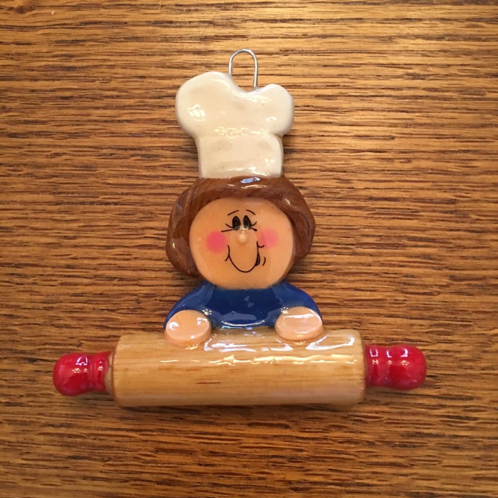 A chef figurine is sitting on top of a rolling pin.
