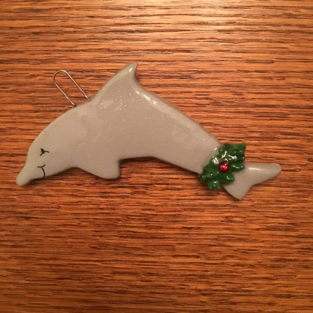 A white dolphin ornament with a green holly leaf.