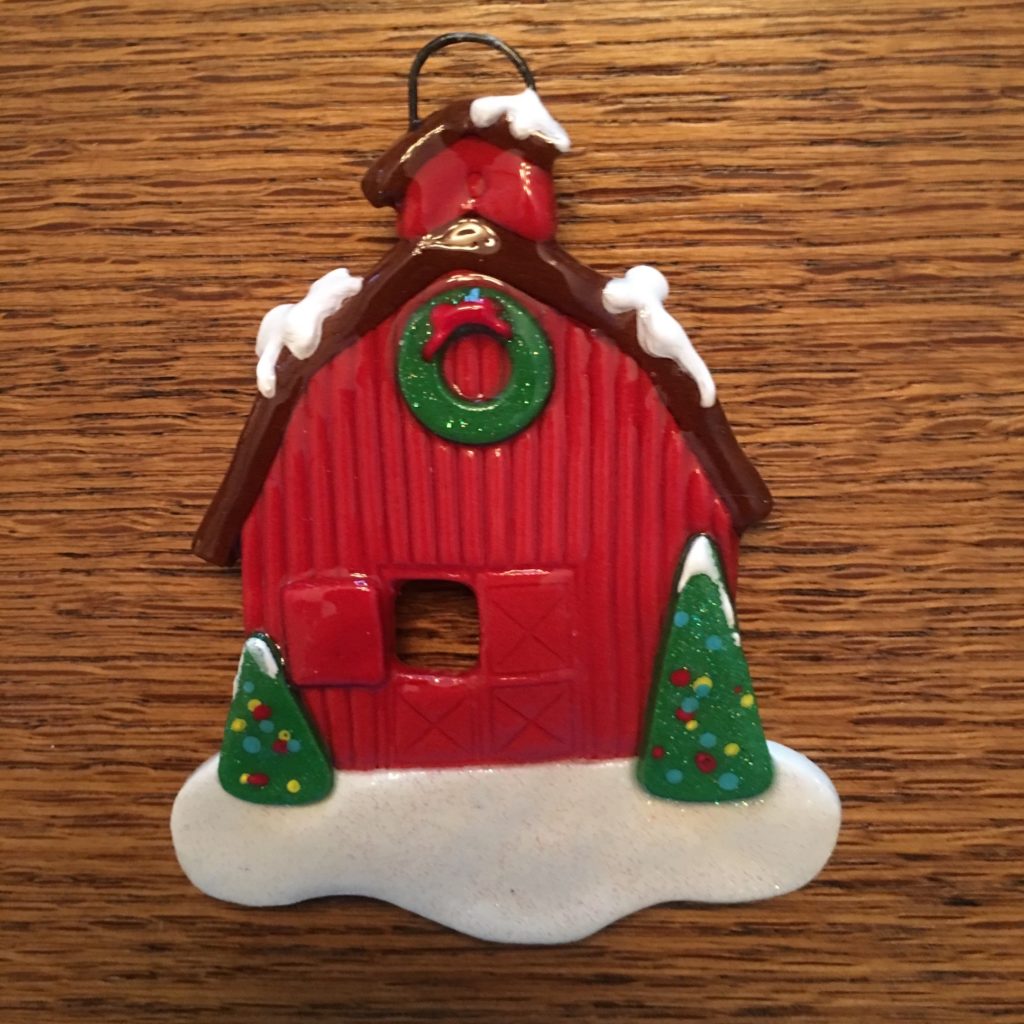 A red barn ornament with snow on top of it.