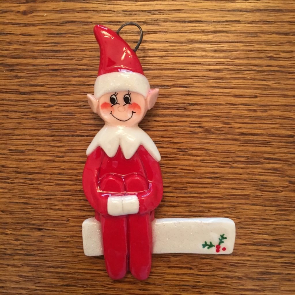 A red elf ornament sitting on top of a wooden table.