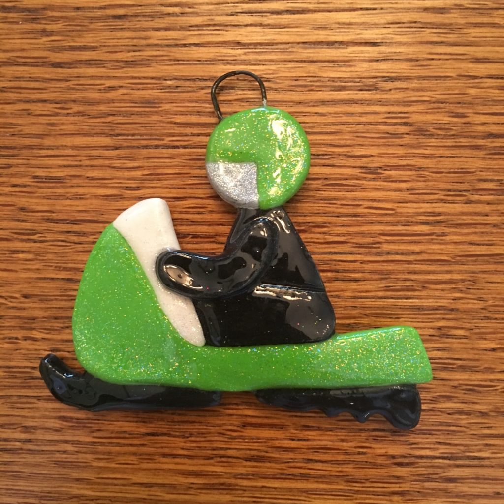 A green and white snowmobile ornament on top of a wooden table.