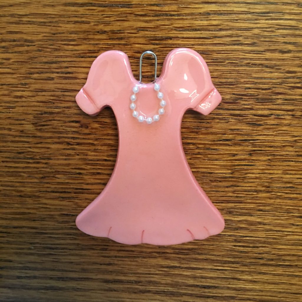 A pink dress shaped paper clip on top of a wooden table.