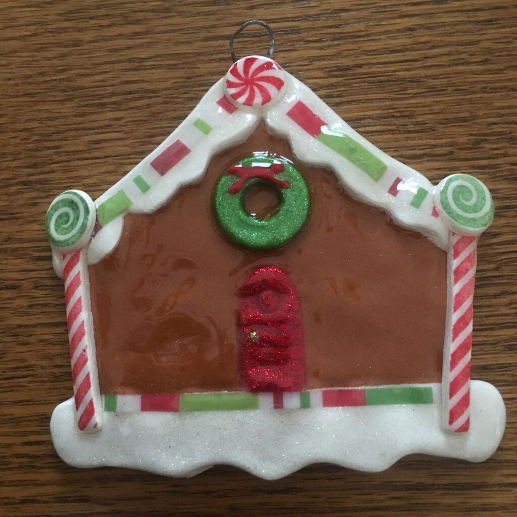 A gingerbread house ornament with candy canes and a wreath.
