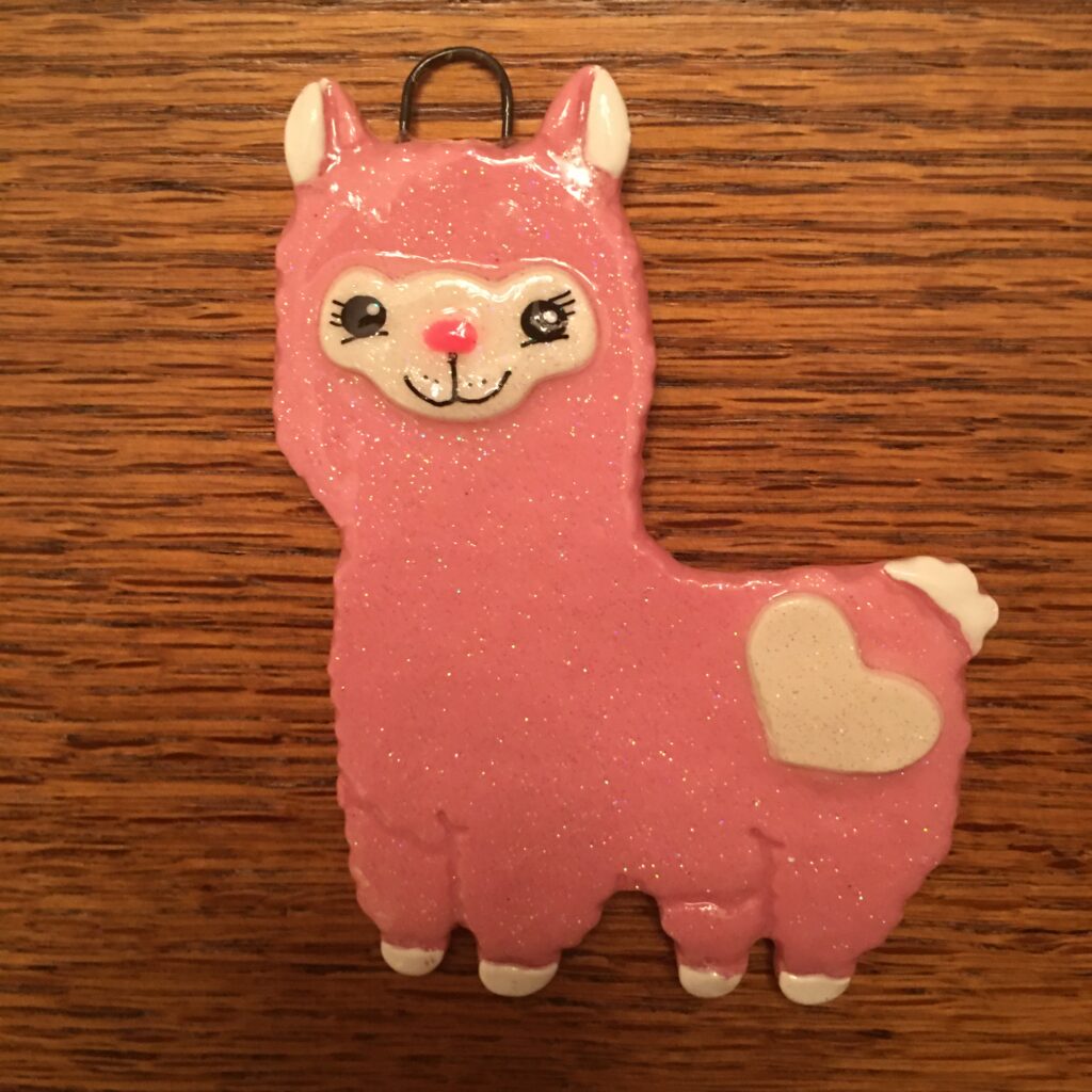 A pink llama ornament sitting on top of a wooden table.