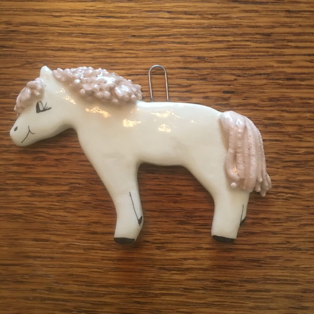 A white horse with pink hair on top of a wooden table.