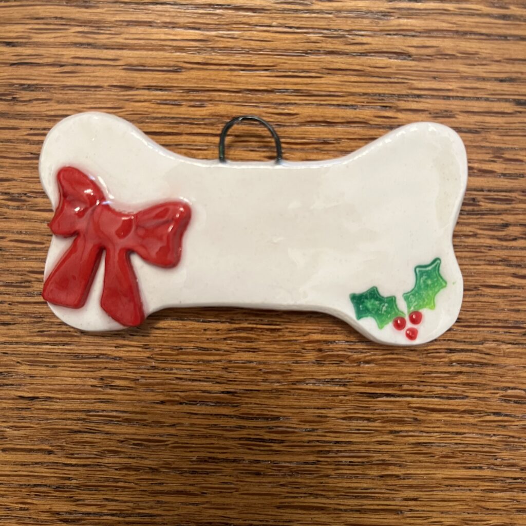 A dog bone ornament with a bow and holly.