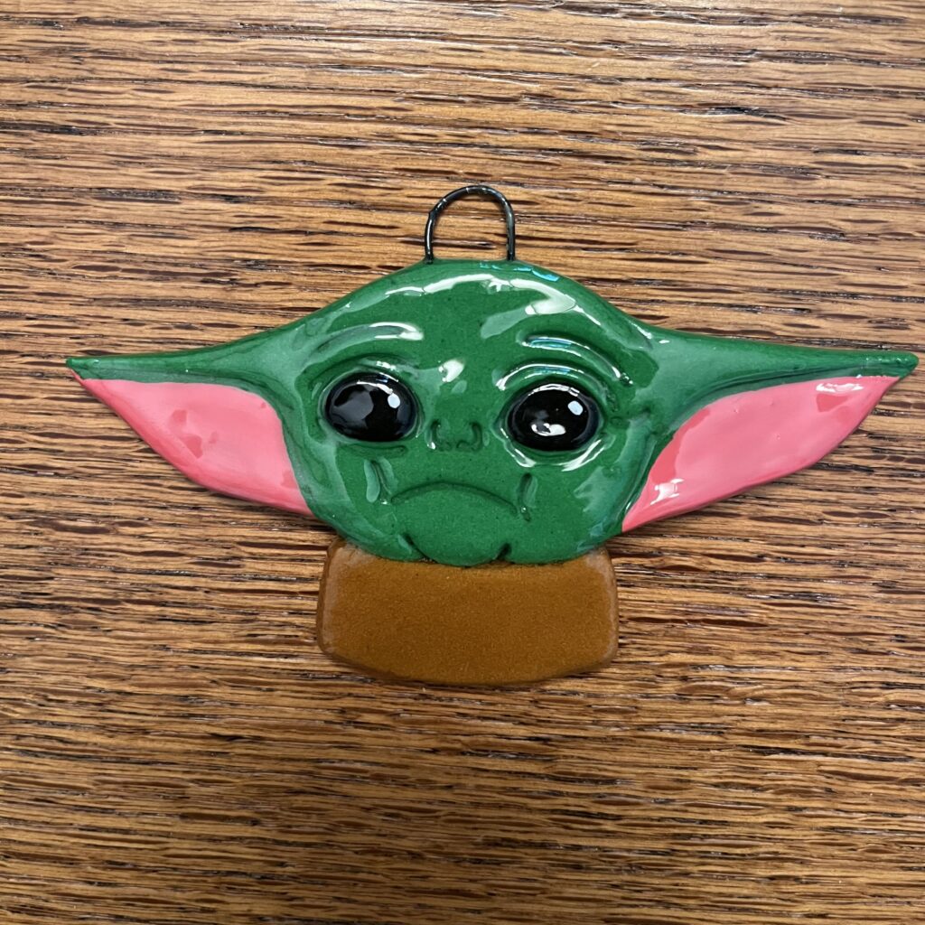 A green baby yoda ornament on top of a wooden table.