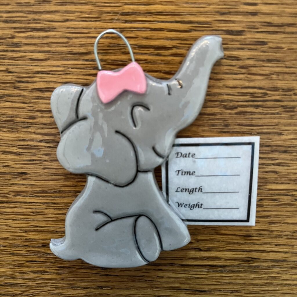 A gray elephant ornament with pink bow and name tag.