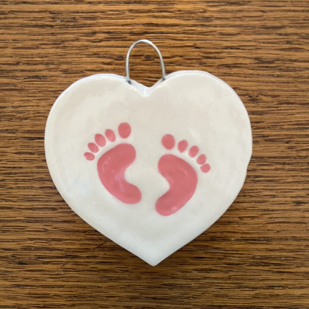 A heart shaped ornament with pink footprints on it.