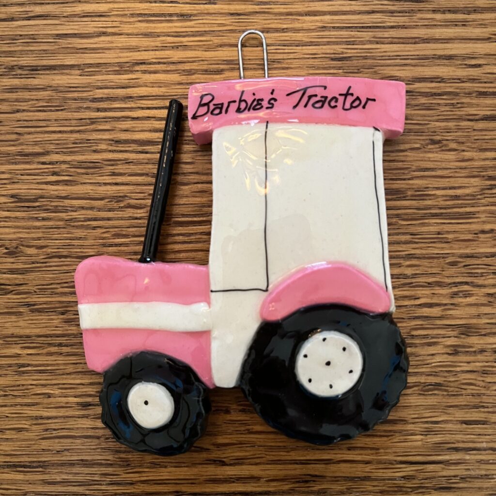 A pink and white tractor ornament on top of a wooden table.